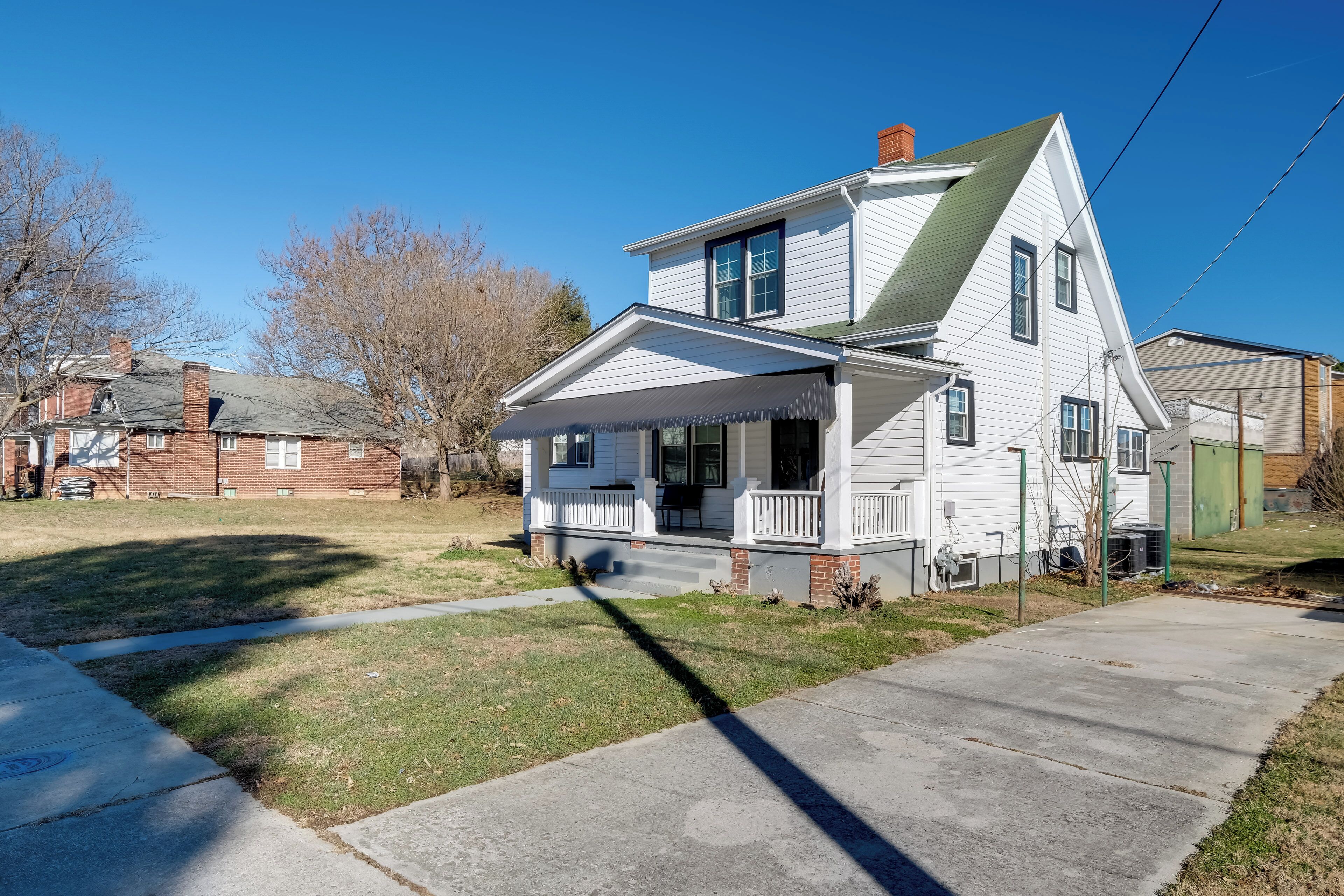 A two-story house with a front porch, a brick chimney, and a green roof.