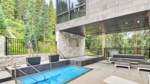 An outdoor pool area with a stone wall, a modern outdoor seating area, and a view of a forested area. - Ski-in/ski-out! Winter Park Family Gem w/ Hot Tub (Winter Park)