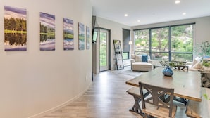 A spacious living area with a large wooden table and chairs, a sofa, and a view of greenery through large windows. - Ski-in/ski-out! Winter Park Family Gem w/ Hot Tub (Winter Park)