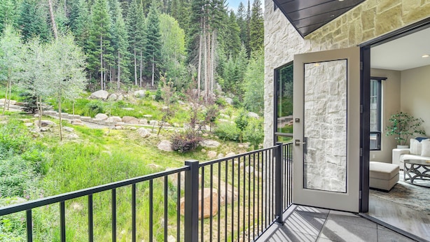 A balcony with a stone wall, a view of a forested hillside, and a seating area with a sofa and coffee table. - Ski-in/ski-out! Winter Park Family Gem w/ Hot Tub (Winter Park)