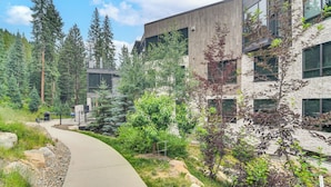 A modern building with a curved pathway, surrounded by dense greenery and tall trees. - Ski-in/ski-out! Winter Park Family Gem w/ Hot Tub (Winter Park)