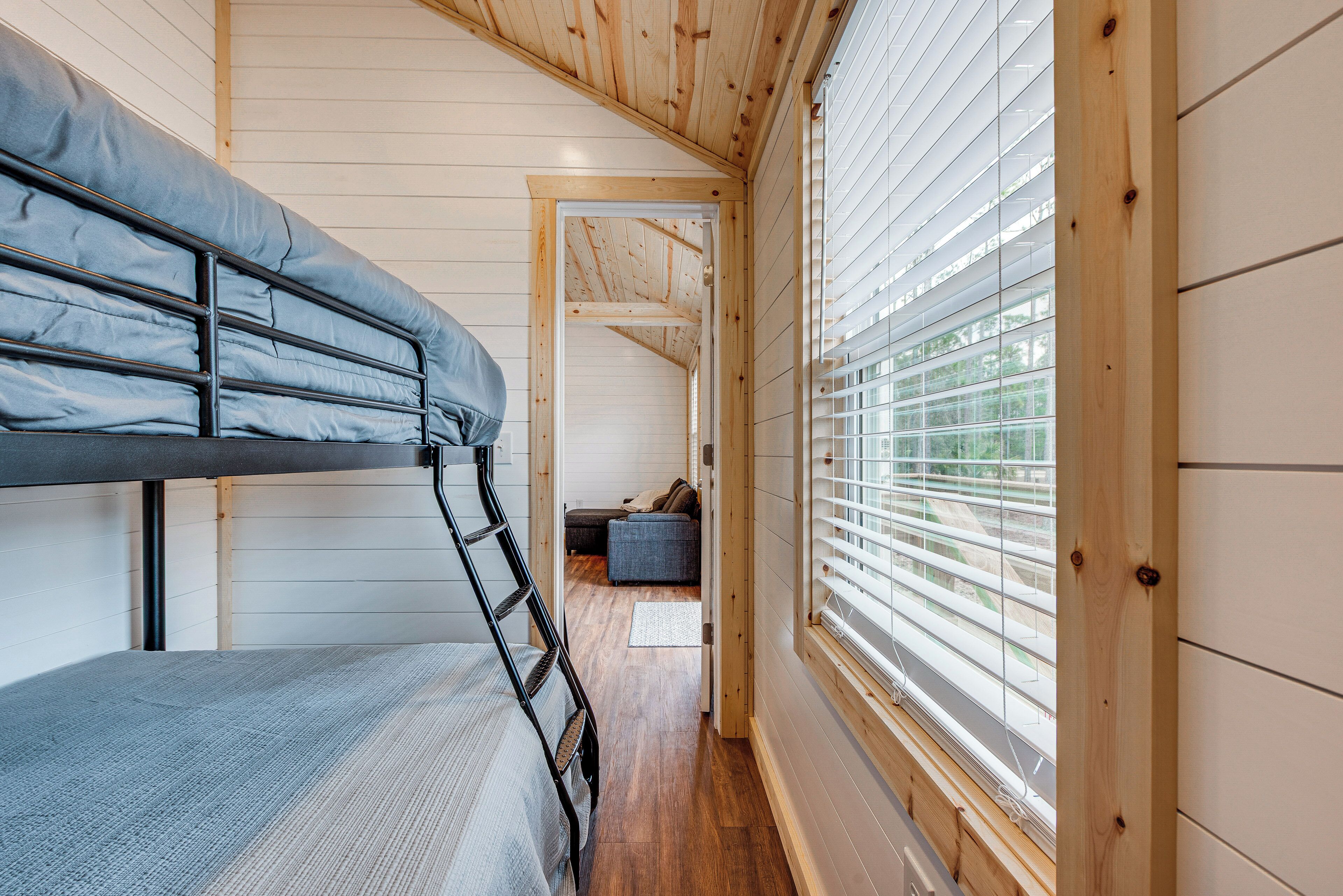 A bunk bed room with a wooden ceiling, a window with blinds, and a hallway leading to another room.