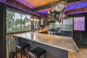 A kitchen with a granite countertop, stainless steel appliances, and a window overlooking a backyard.