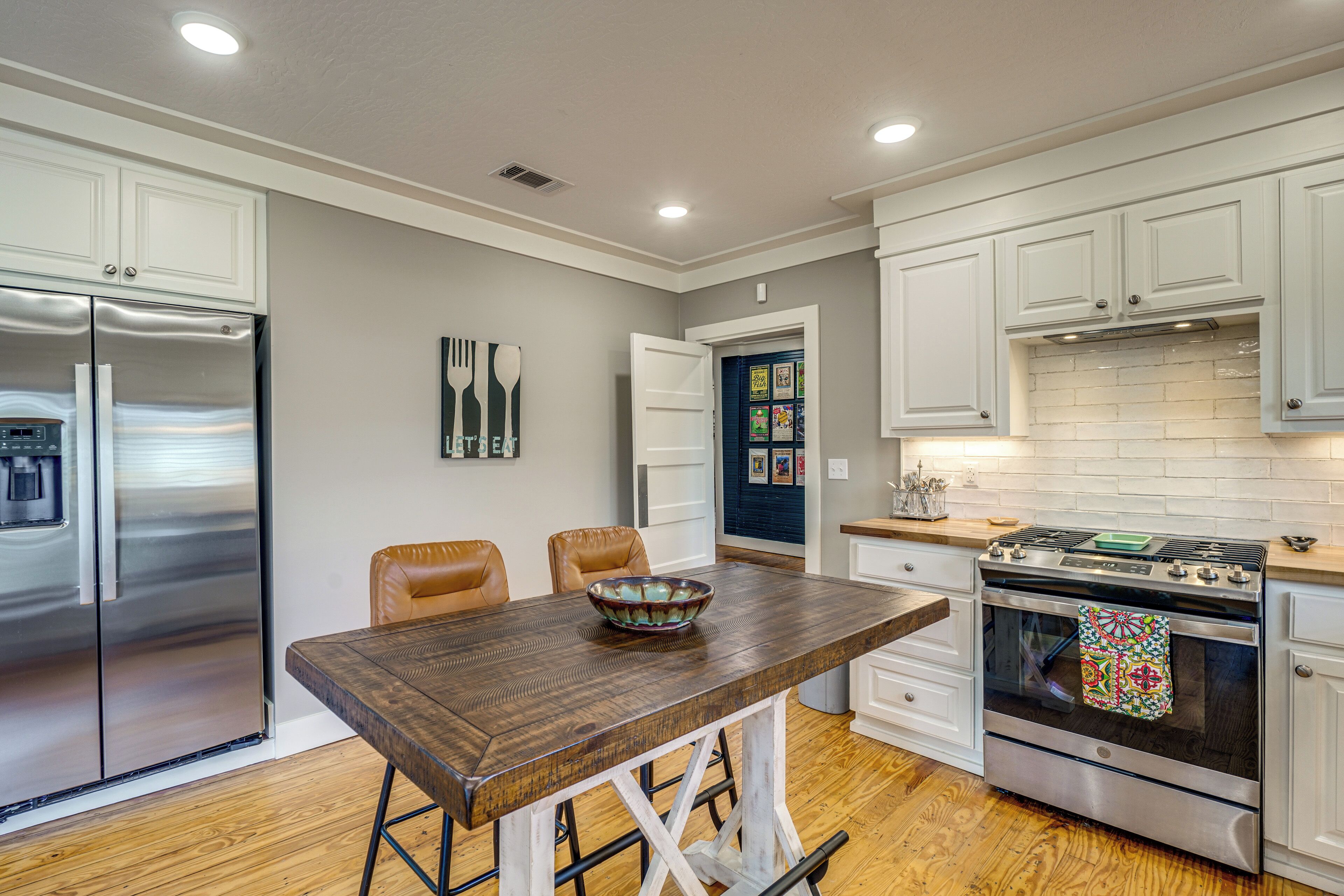 Una cocina moderna con armarios blancos, electrodomésticos de acero inoxidable, una mesa de madera y un salpicadero decorativo.