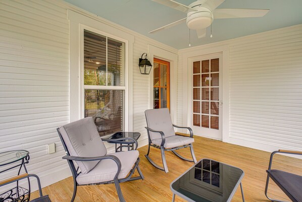 A covered porch with white siding, a ceiling fan, and a glass table.
