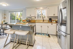 A modern kitchen with white cabinets, a stainless steel refrigerator, and a bar area with stools. - 2 Mi to Wineries! Woodinville Home w/ Deck & Yard (Woodinville)