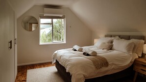 Quarto com uma cama grande, uma mesa de cabeceira, um espelho e uma janela com ar condicionado.