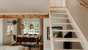 Uma área de jantar com teto de madeira, mesa de jantar com cadeiras, luminária pendente e janela com cortinas.