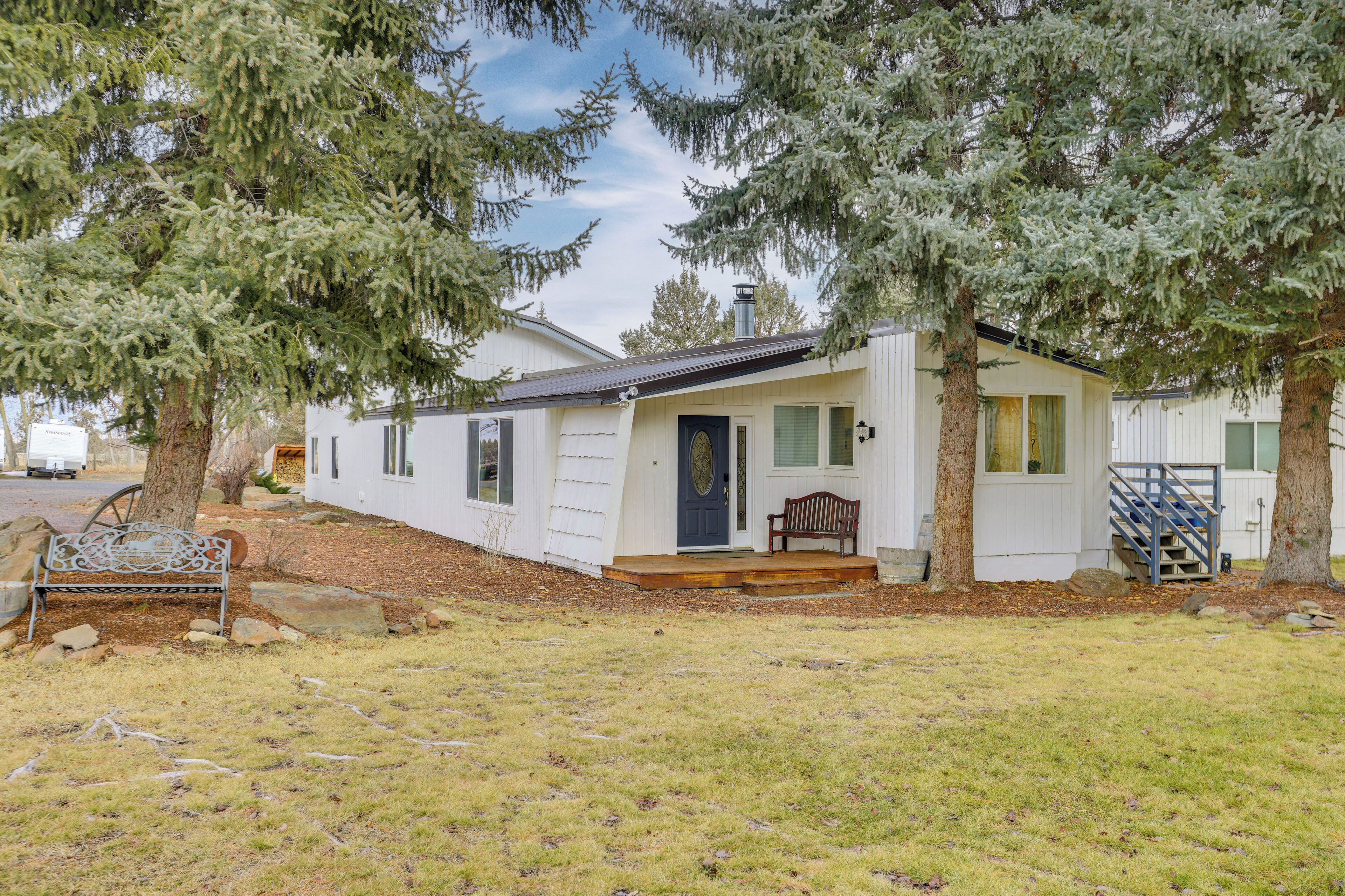 A single-story mobile home with a front porch, a bench, and a staircase leading to a deck.