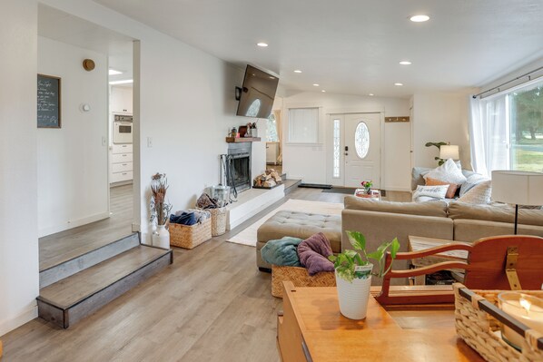 A modern living room with a fireplace, a sofa, a dining table, and a kitchen area visible through an open door. - Stunning Mountain Views! Secluded Retreat in Bend (Bend)