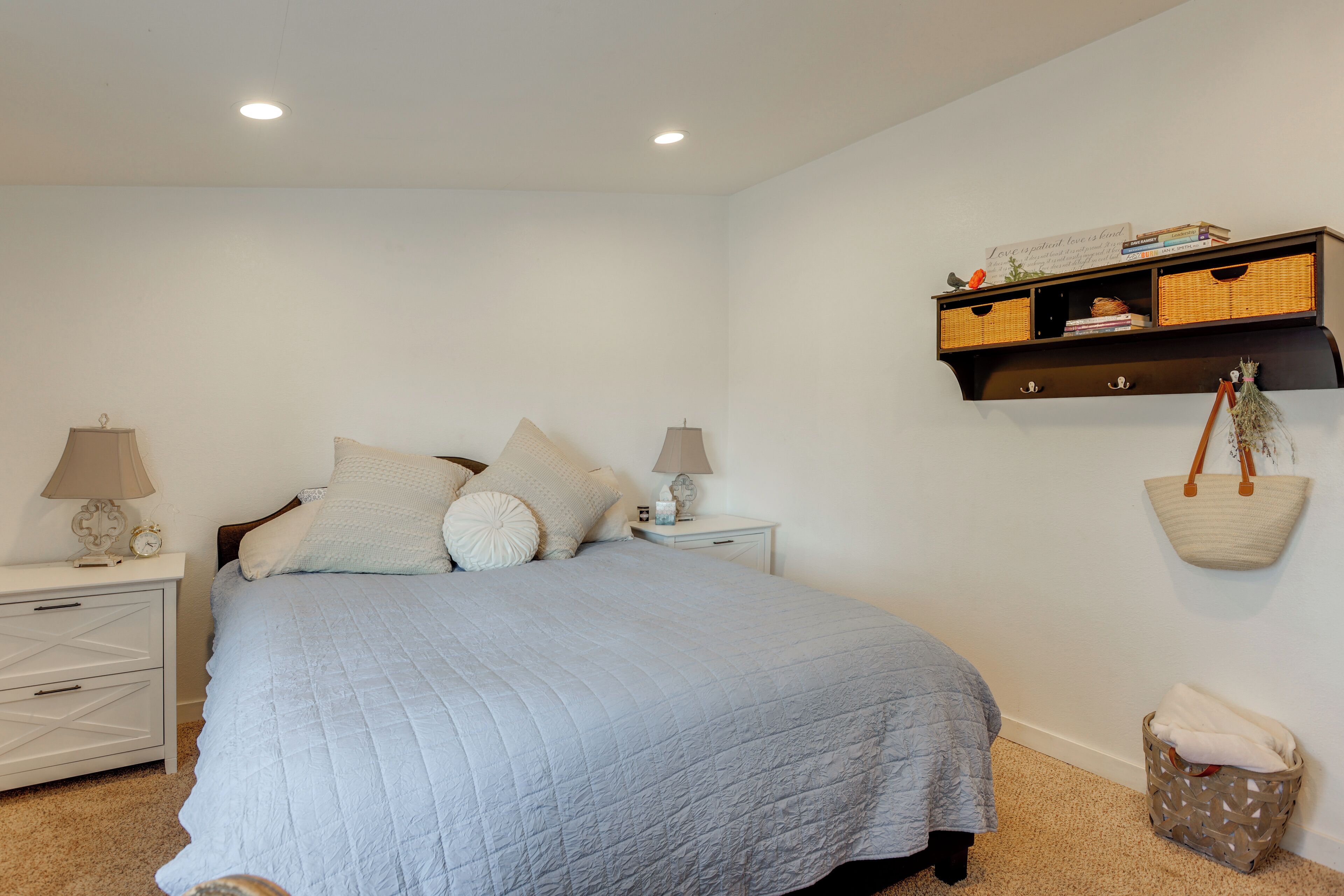 Une chambre à coucher comprenant un lit, des tables de chevet, une étagère fixée au mur et un panier suspendu.