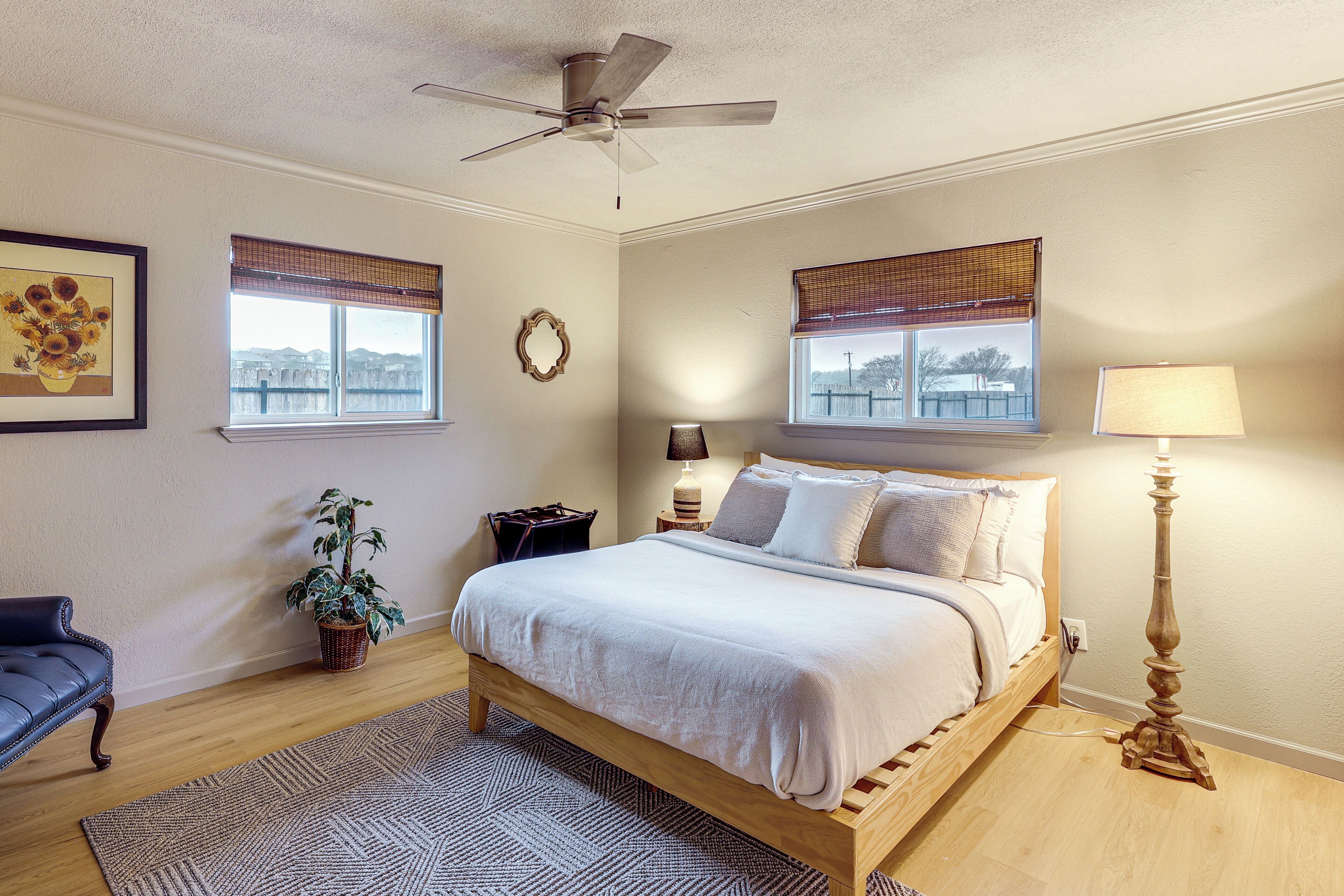 A bedroom with a bed, a ceiling fan, a window with a view, a lamp, and a plant.