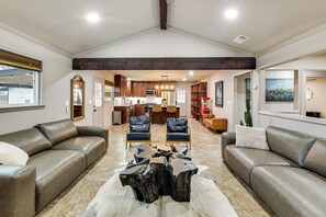 A spacious living area with leather sofas, a central coffee table, and a kitchen in the background.