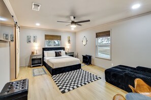 A bedroom with a bed, bedside tables, a ceiling fan, a black couch, and a window with blinds.