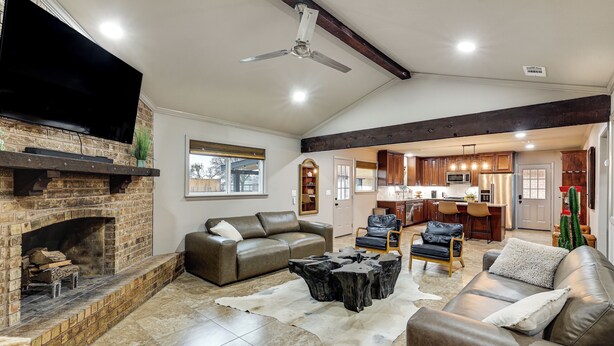 A spacious living room with a fireplace, leather sofas, a coffee table, and a view into the kitchen. - Private Patio & Yard: Pet-friendly Bulverde Home (Bulverde)