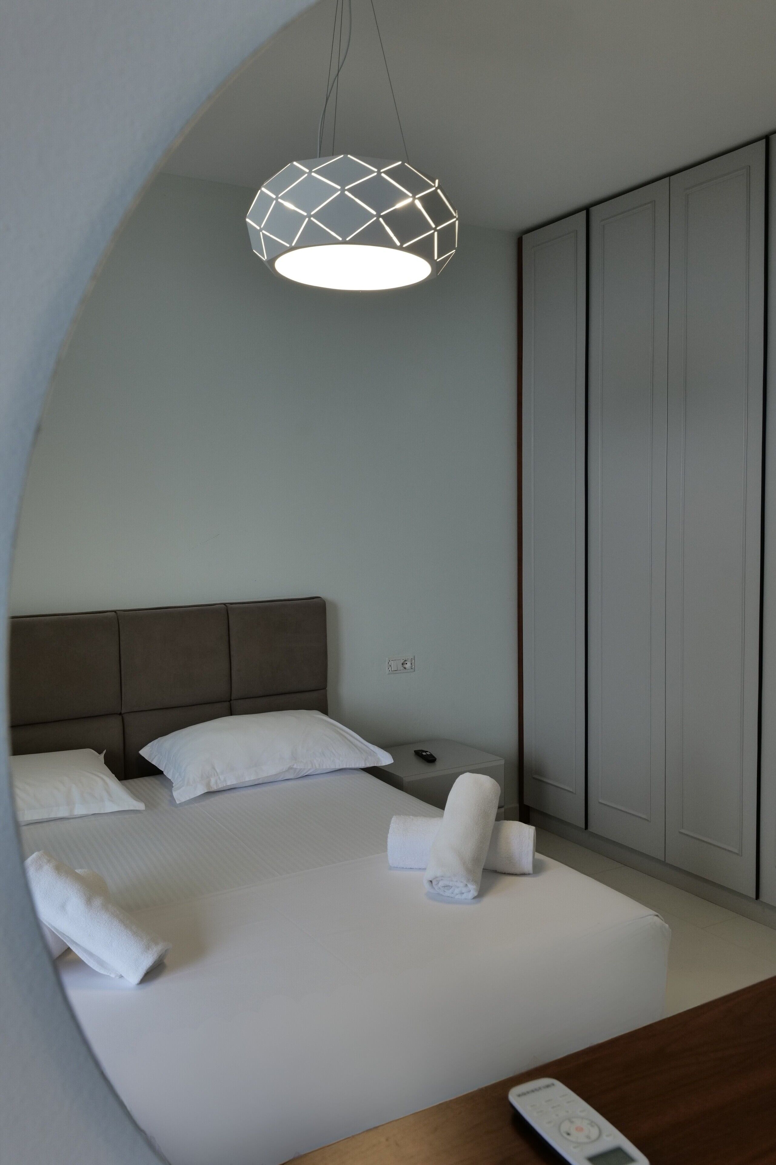 A modern hotel room with a bed, a nightstand, a remote control, and a wardrobe.