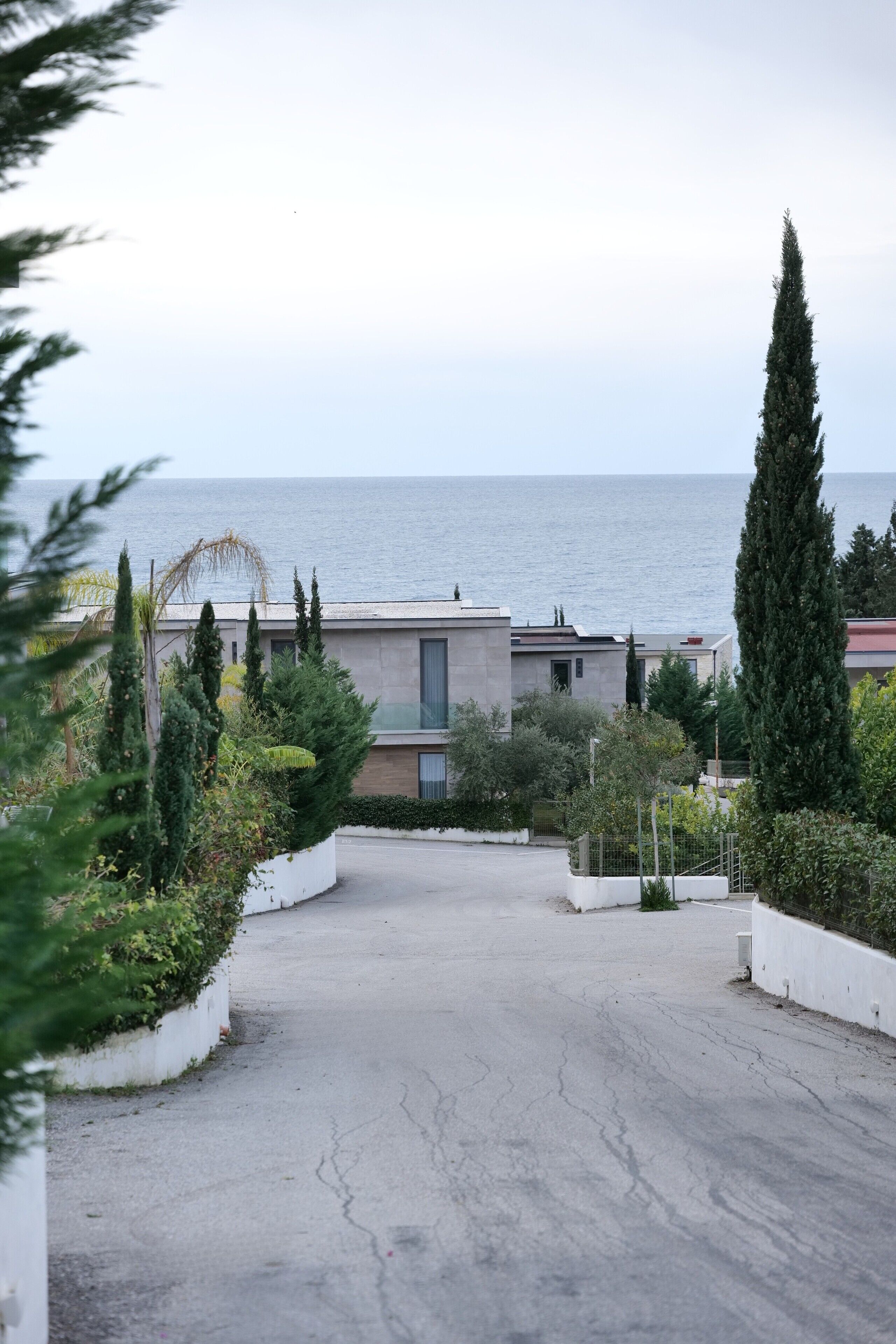 A residential area with a paved driveway leading to a modern house with a view of the sea.