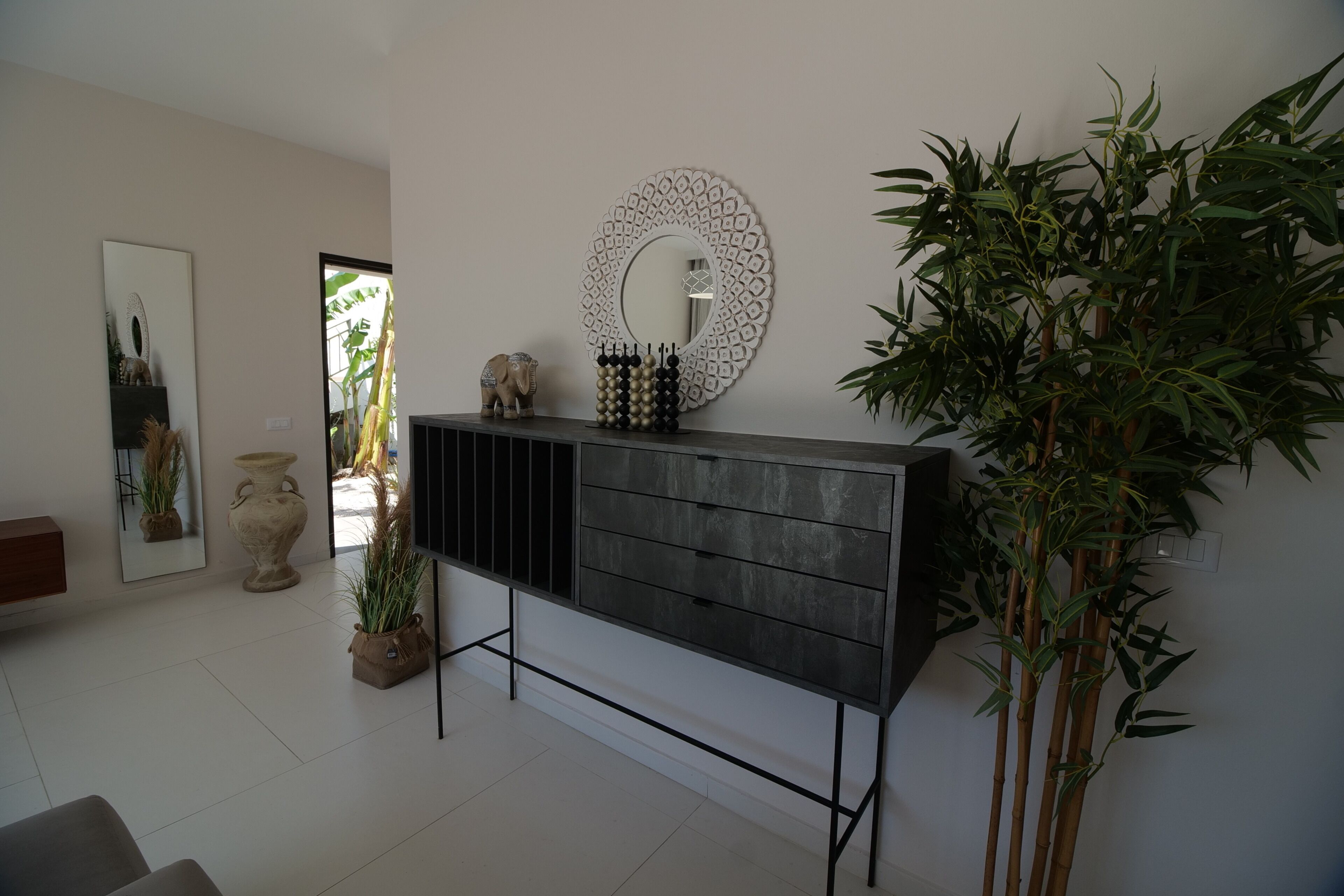 A modern living room with a dark wooden console, a decorative mirror, and a large bamboo plant.