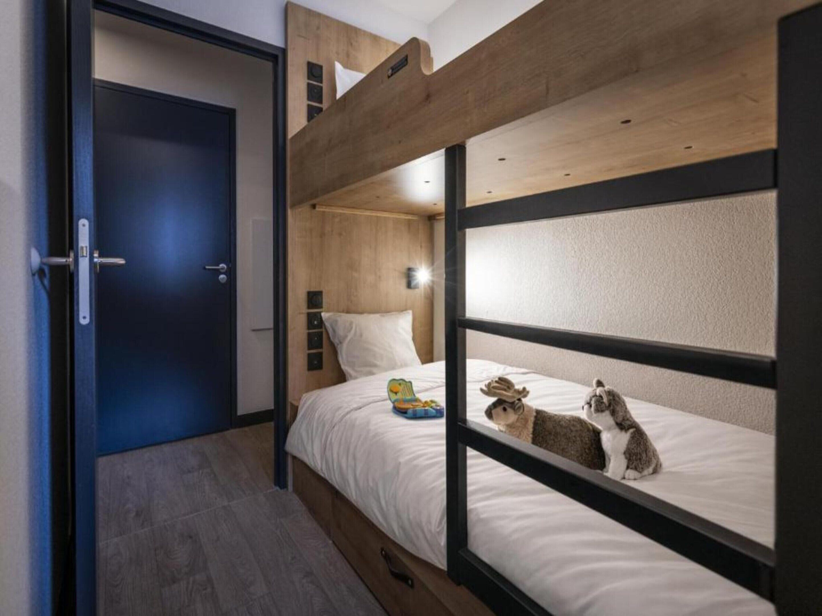 Et soveværelse med køjeseng, en dør, et lille bord med lampe og en hylde på væggen.