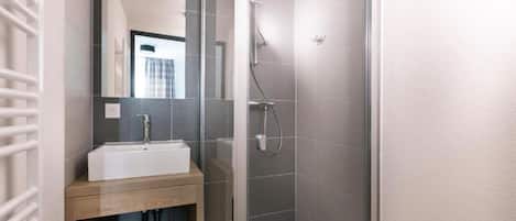 Une salle de bain moderne avec une douche à l’italienne en verre, un lavabo blanc et un meuble-vasque en bois.