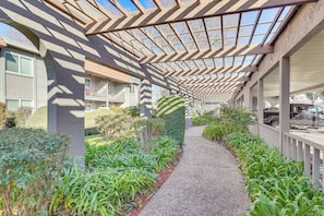 A covered walkway with a patterned ceiling, surrounded by greenery and a gravel path.