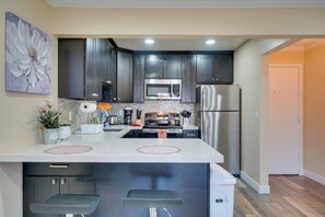 A modern kitchen with dark cabinets, stainless steel appliances, and a central island with bar stools. - Sip, Golf & Explore: Pleasanton Retreat! (Pleasanton)