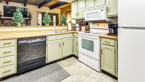 A kitchen with a dishwasher, stove, microwave, and refrigerator. There are Christmas trees and a flat-screen TV on the wall. - Nat'l Forest Retreat at 'the Nest at Pinetop' (Pinetop)