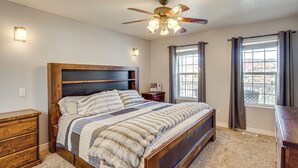 A bedroom with a large bed, wooden headboard, ceiling fan, bedside tables, and a window with curtains. - Family & Group Friendly! Hilltop Cedar City Home (Cedar City)
