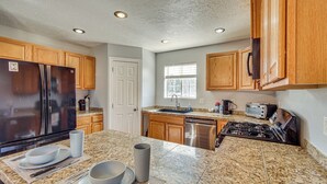 A kitchen with granite countertops, wooden cabinets, a stainless steel refrigerator, a dishwasher, and a gas stove. - Family & Group Friendly! Hilltop Cedar City Home (Cedar City)