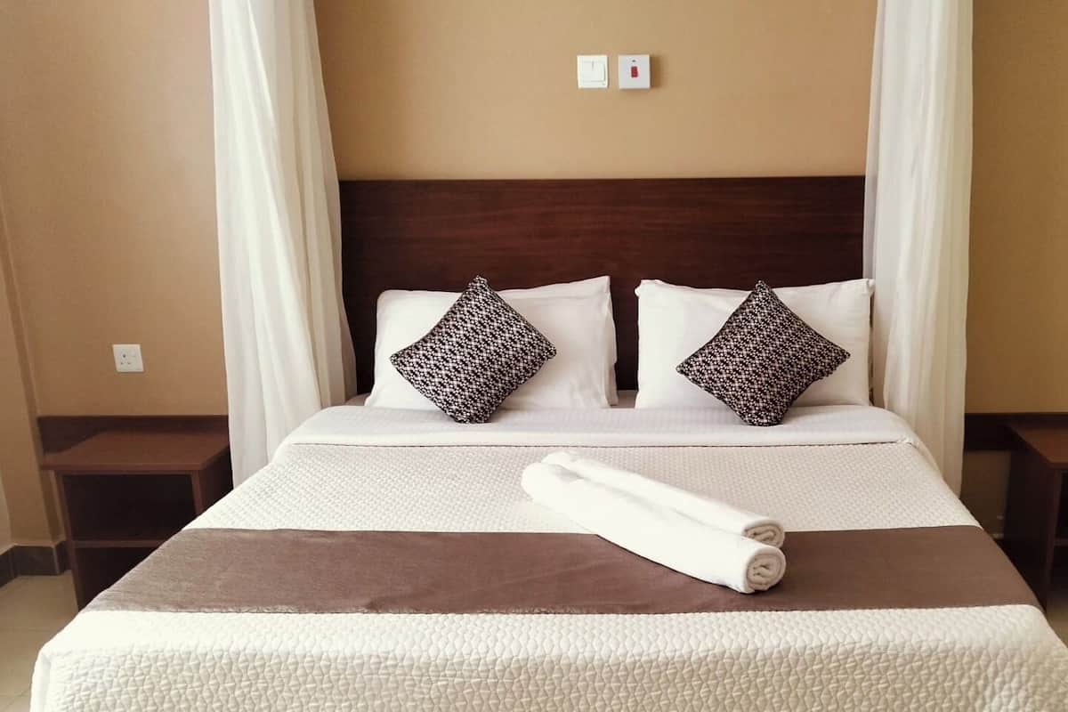 Cama bem arrumada com colcha estampada, duas almofadas e uma toalha enrolada.