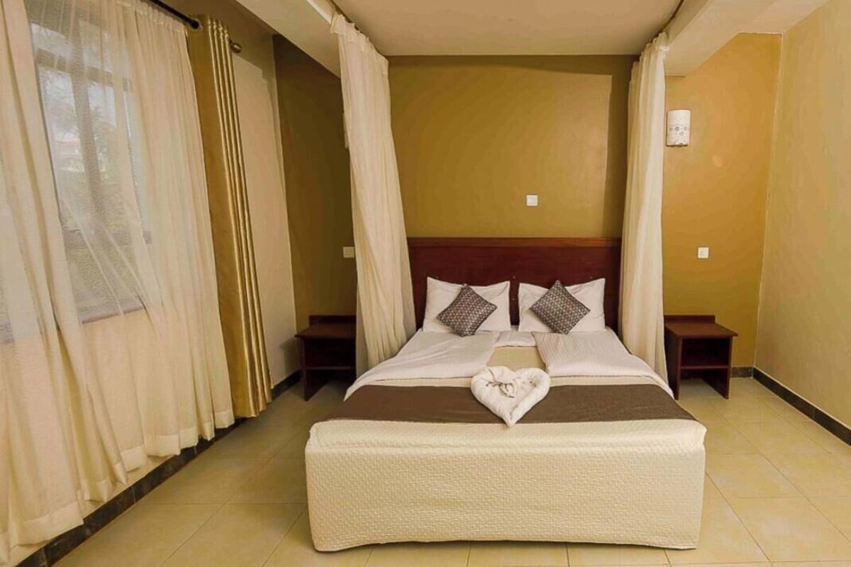 Quarto de hotel com uma cama grande, um travesseiro em formato de coração e cortinas.