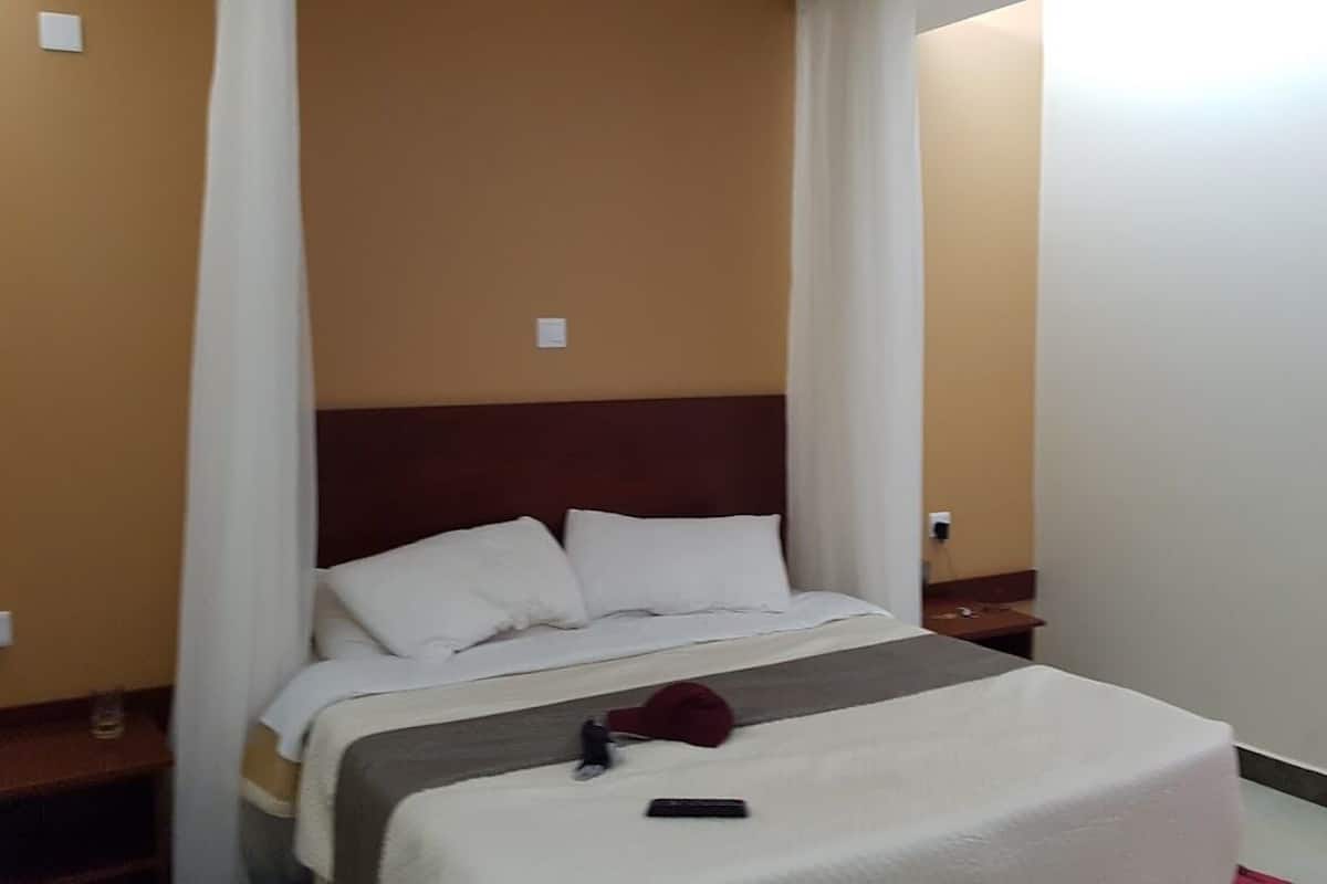 Quarto de hotel com uma cama, mesa de cabeceira e cortina.