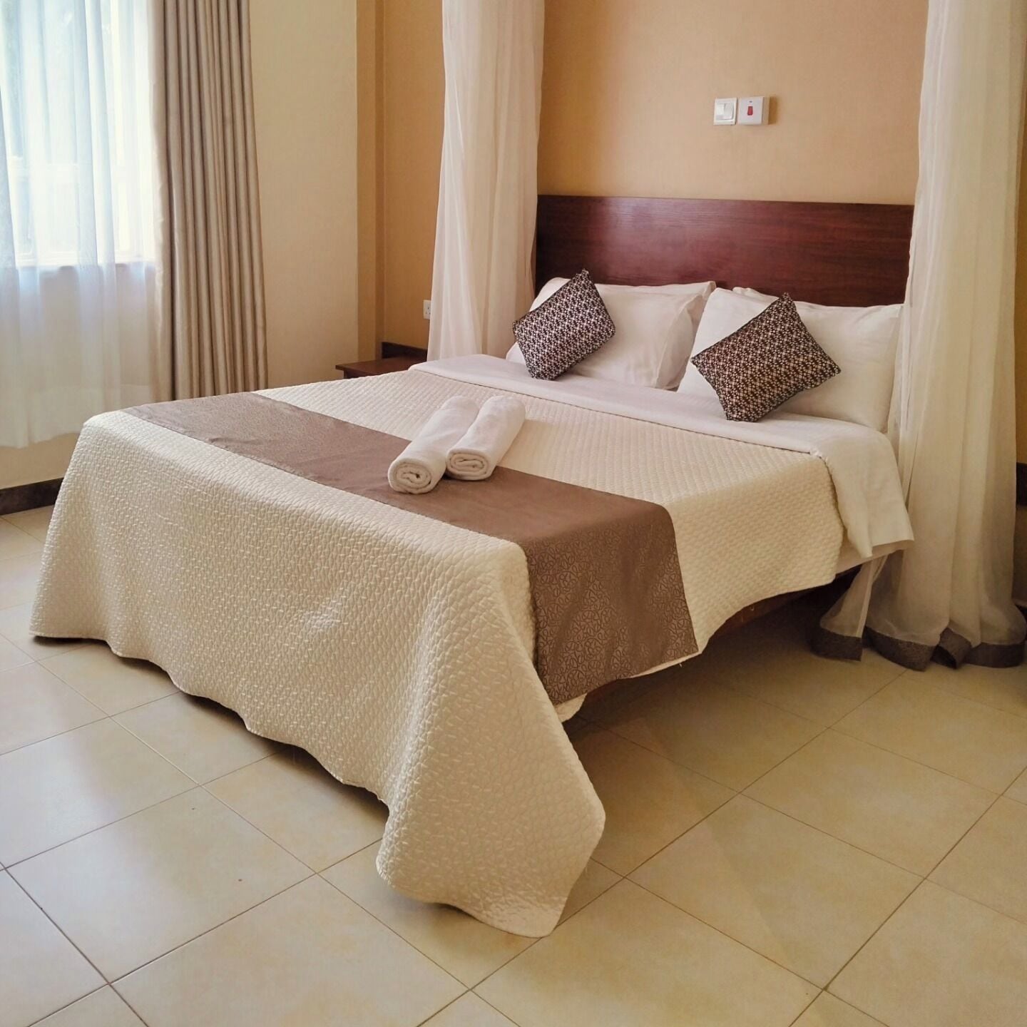 A neatly made bed with a brown and white bedspread, two rolled towels, and patterned pillows.