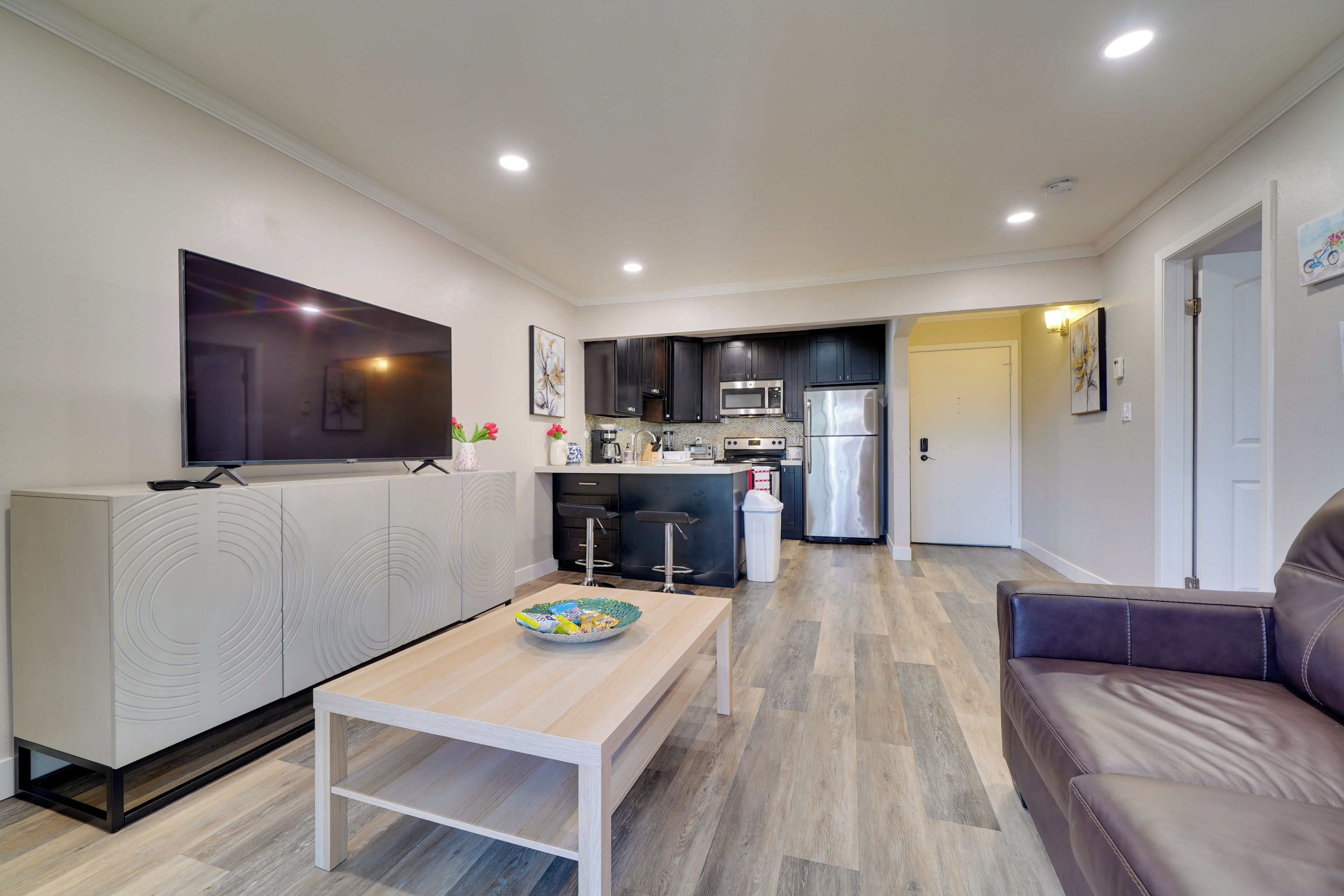 A modern kitchen with dark cabinets, a microwave, and a refrigerator. There is a dining area with a table and a sofa.