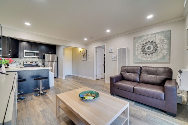 A modern kitchen with dark cabinets, a microwave, and a refrigerator. There's a dining area with a brown leather couch and a wooden coffee table. - Pleasanton Gem in Quiet Community w/ Pool Access (Pleasanton)