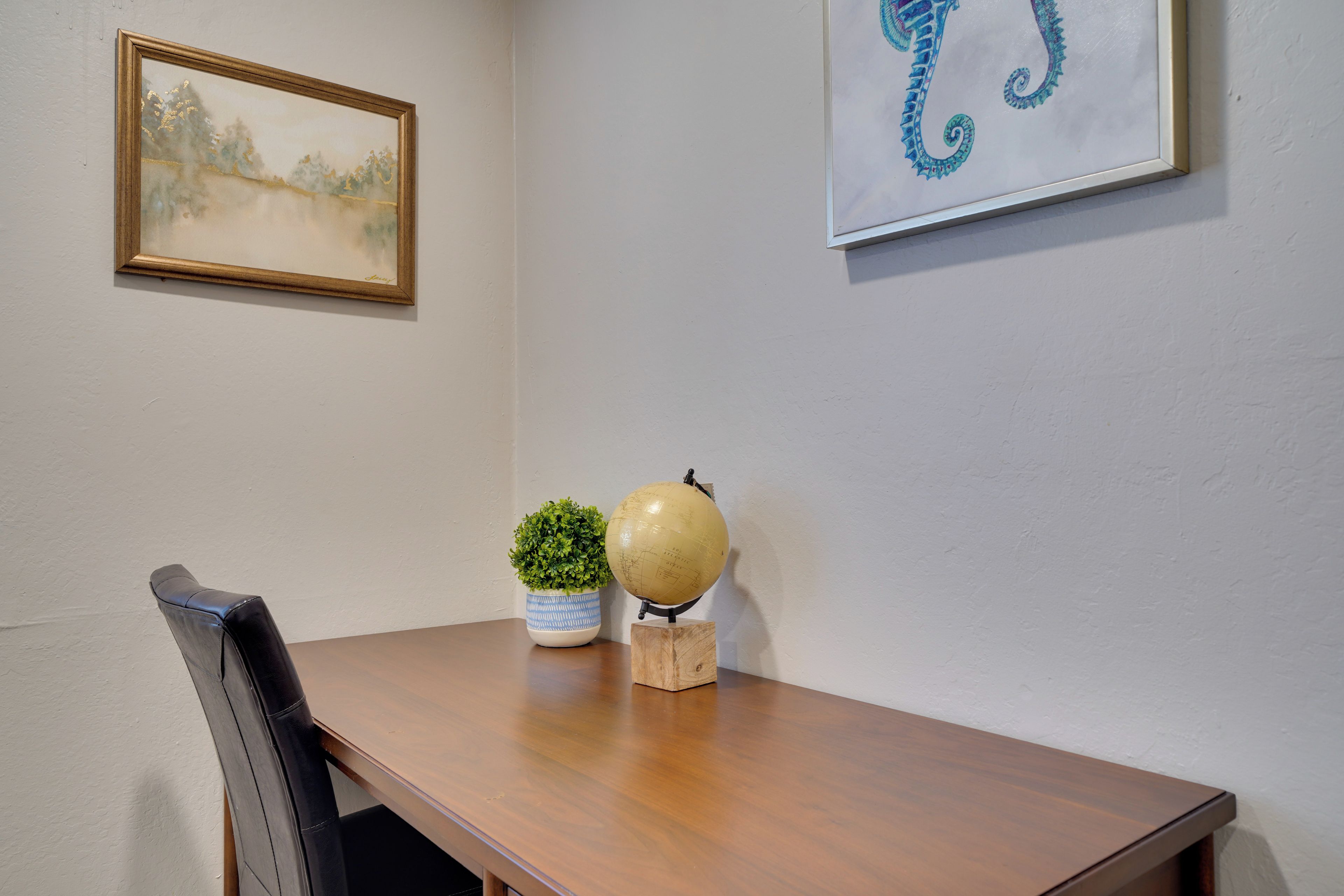 Ein Holztisch mit Globus und Topfpflanze, ein gerahmtes Bild an der Wand und ein Stuhl im Vordergrund.