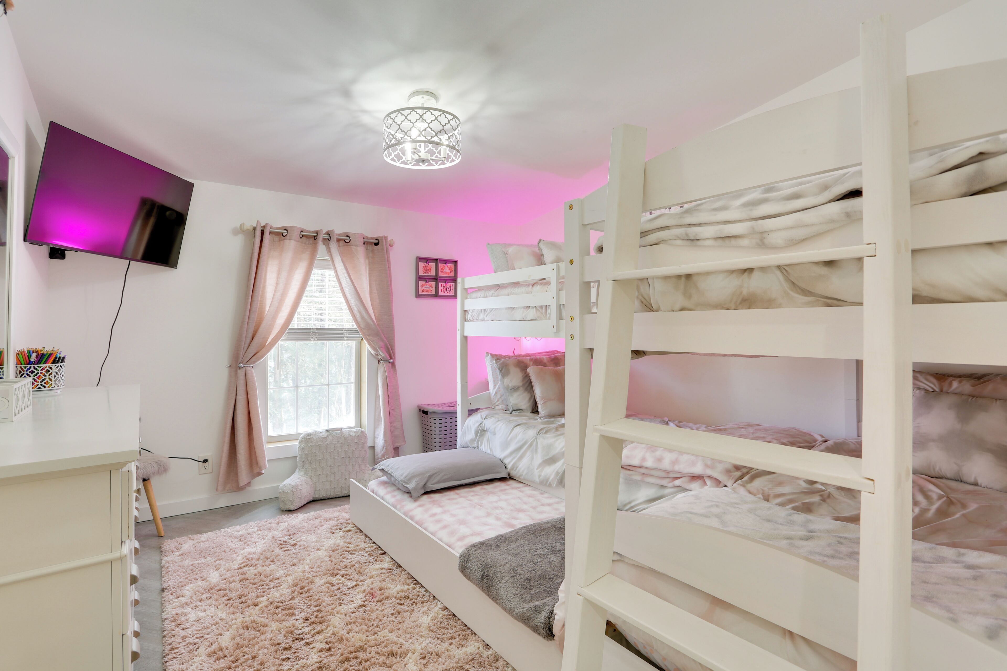 A bedroom with bunk beds, a TV, a ceiling light, a window with curtains, and a fluffy rug.