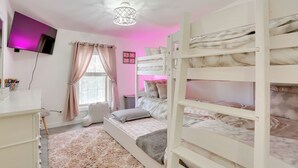 A bedroom with bunk beds, a TV, a ceiling light, a window with curtains, and a fluffy rug.