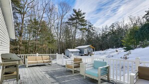 A wooden deck with outdoor furniture, a white fence, and a cabin in a snowy forest.