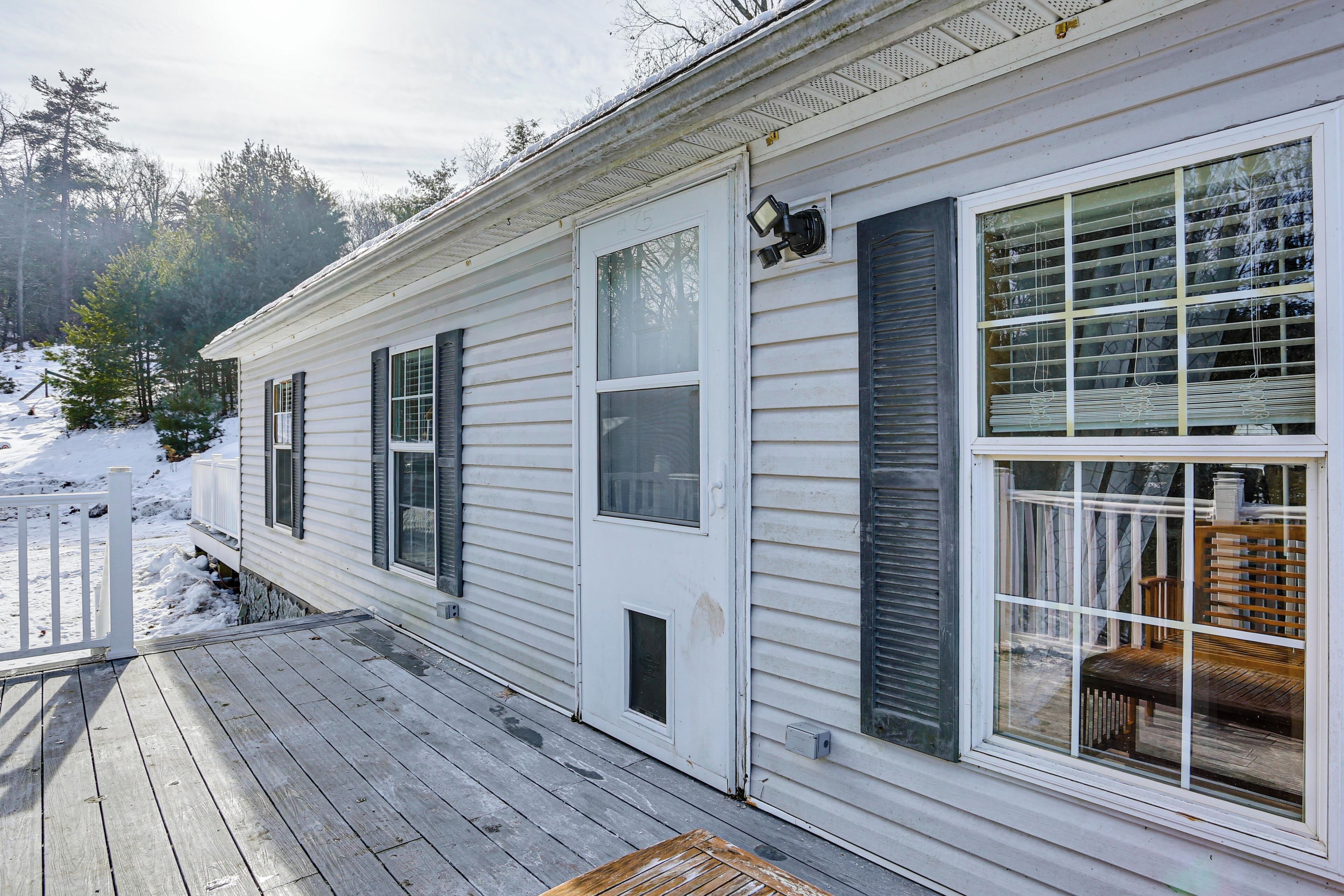 A white house with a wooden deck and a large window with blinds.