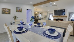 A dining area with a wooden table set for four, a kitchen in the background, and a TV mounted on the wall.