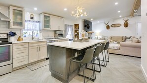 A modern kitchen with a central island, bar stools, and a chandelier.
