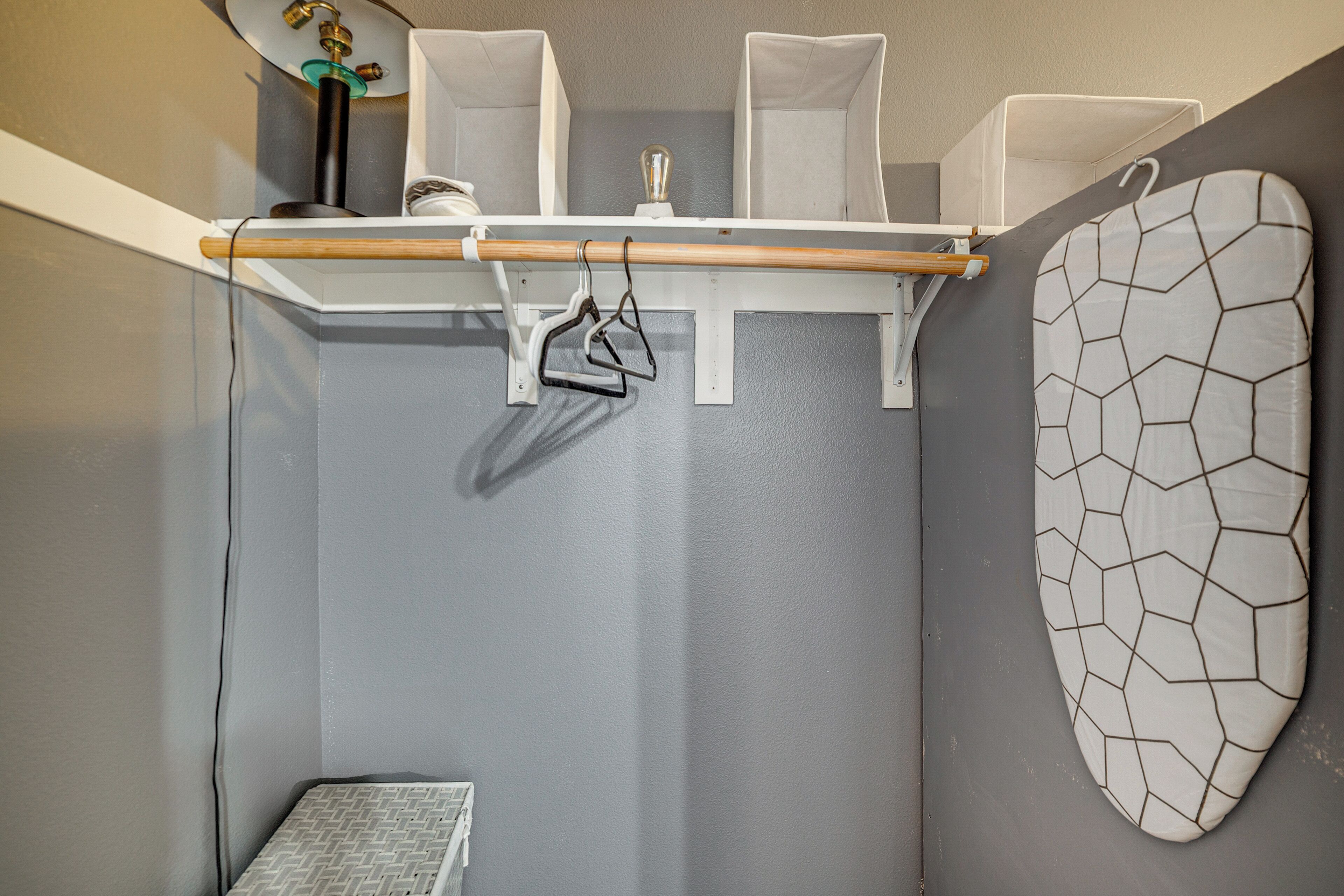 Un baño con pared gris, toallero blanco, repisa blanca con lámpara y espejo blanco de diseño geométrico.