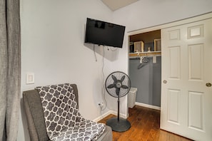 A room with a television mounted on the wall, a standing fan, a patterned armchair, and a white door. - Sip, Hike & Explore: Quiet Socal Studio w/ Patio! (Winchester)