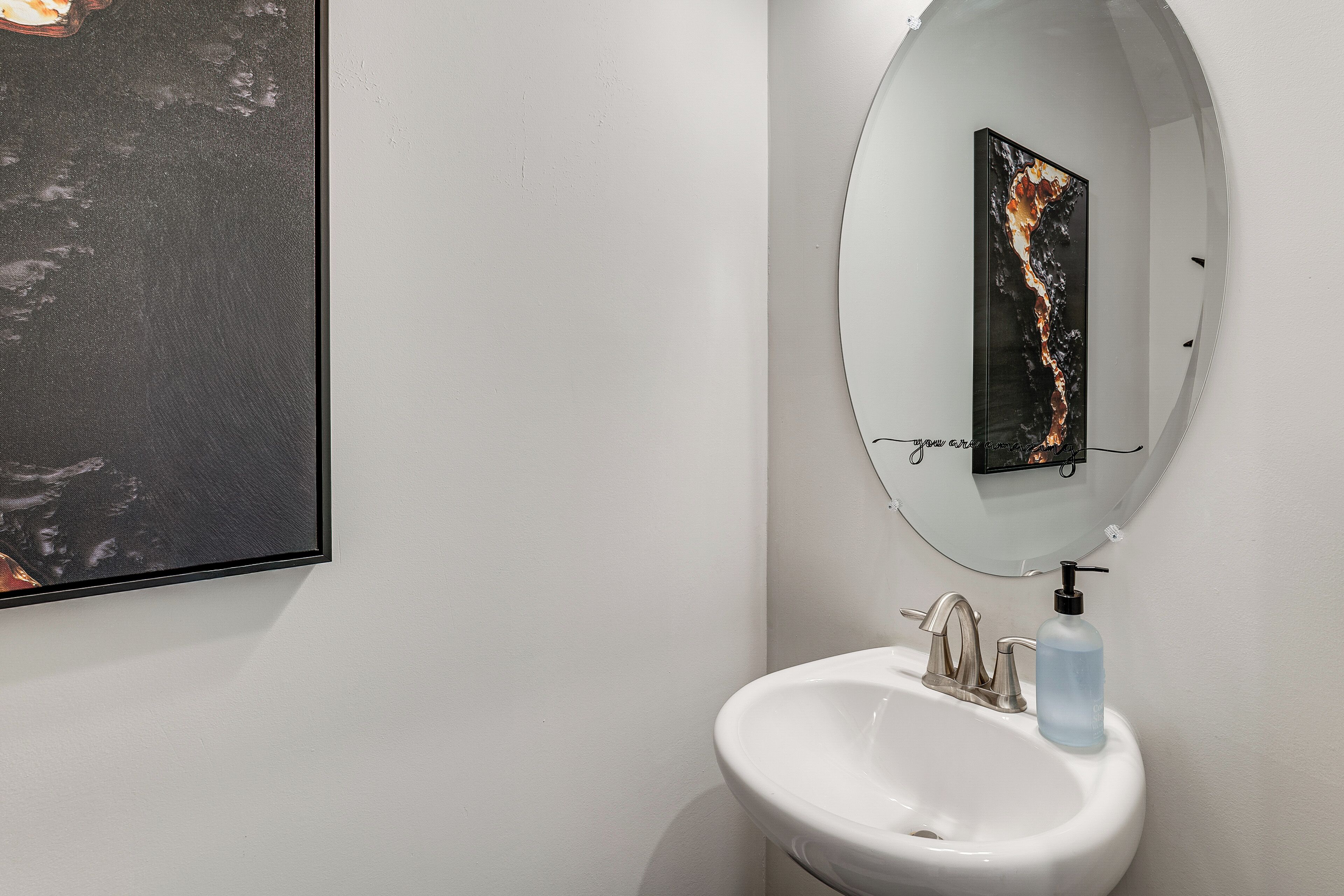 A bathroom with a white sink, a mirror, and a framed abstract painting on the wall.