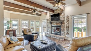 A spacious living room with leather sofas, a stone fireplace, and large windows. - 2-tier Dock! Jordan Lake Family Retreat (Titus)