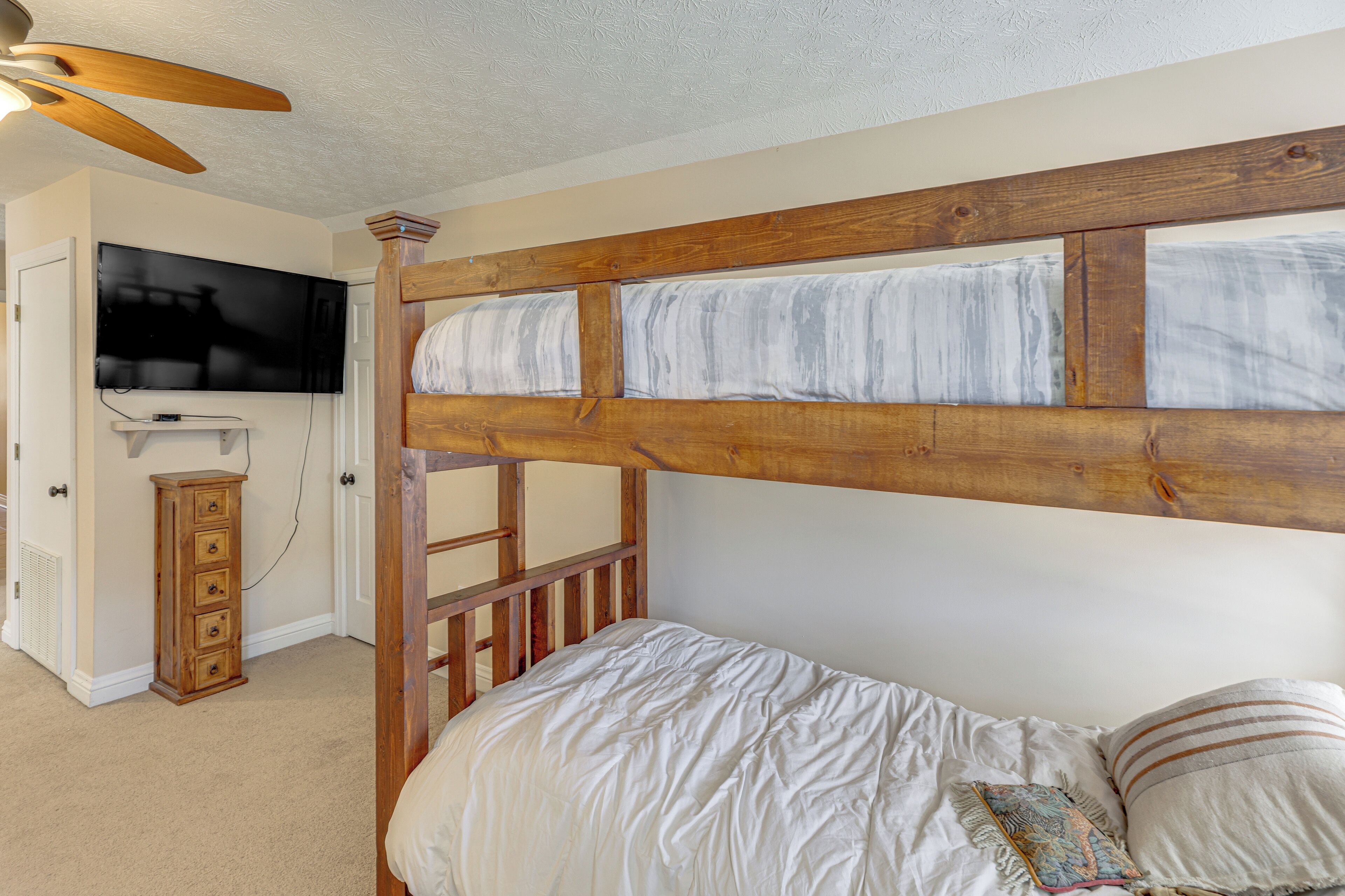 Ein Schlafzimmer mit Etagenbett, einem an der Wand befestigten Fernseher und einer hölzernen Kommode.