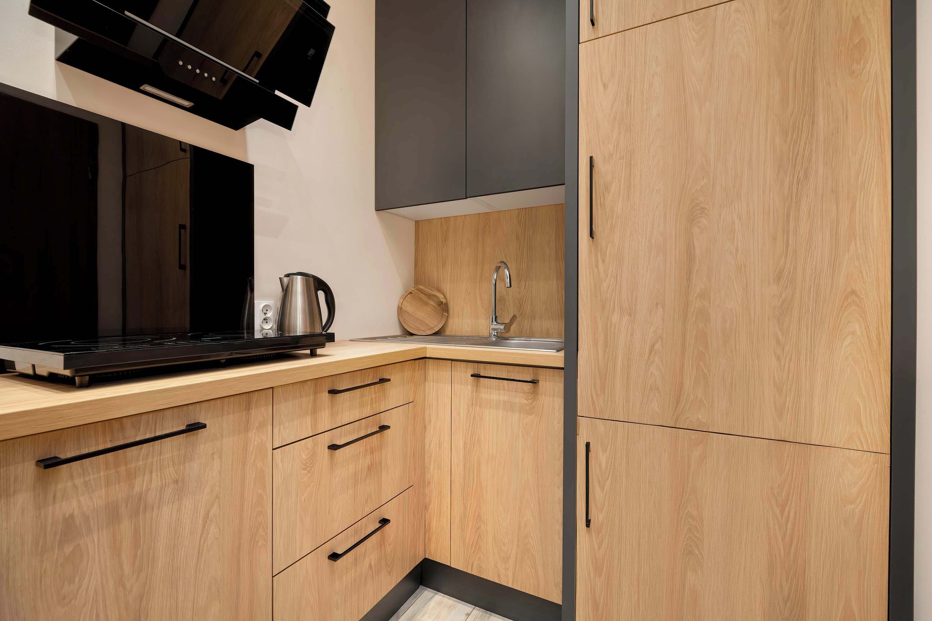 A modern kitchen with a black stove, stainless steel kettle, and a wooden countertop.