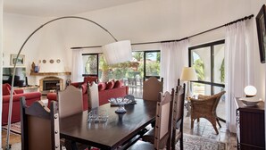 A spacious living area with a fireplace, red sofas, a dining table with chairs, and large windows offering a view of the outdoors. - Casa Rouxinol in Carvoeiro (Lagoa)