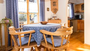 A dining area with a round table, four wooden chairs, and a blue tablecloth. - Landhaus Albrecht - Holiday apartment 03 (51 m²) for 2 guests with 2 balconies (Mittenwald)